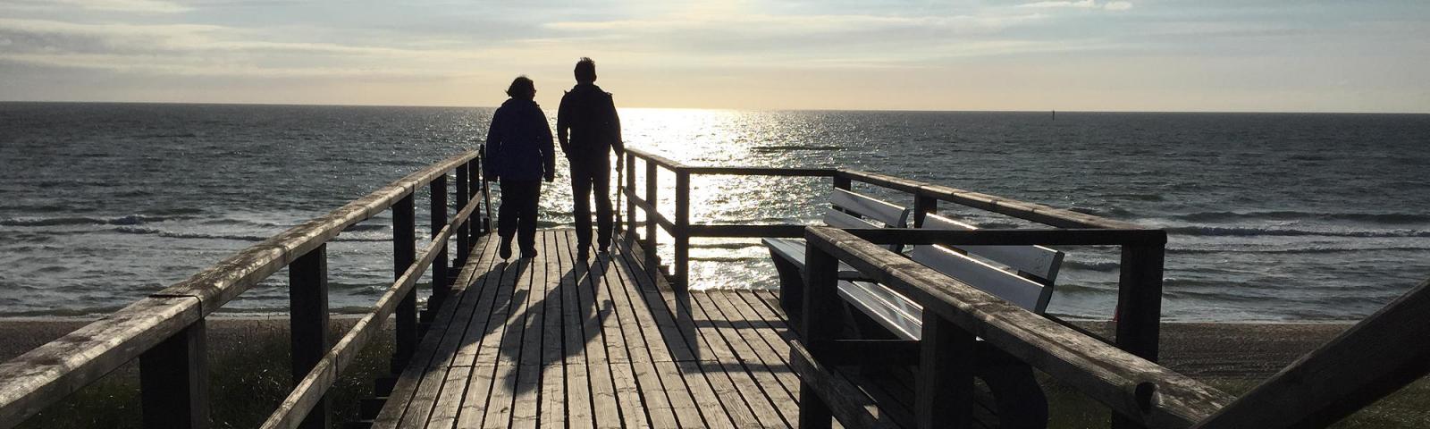 Zwei Personen im Gegenlicht schauen auf das Meer.